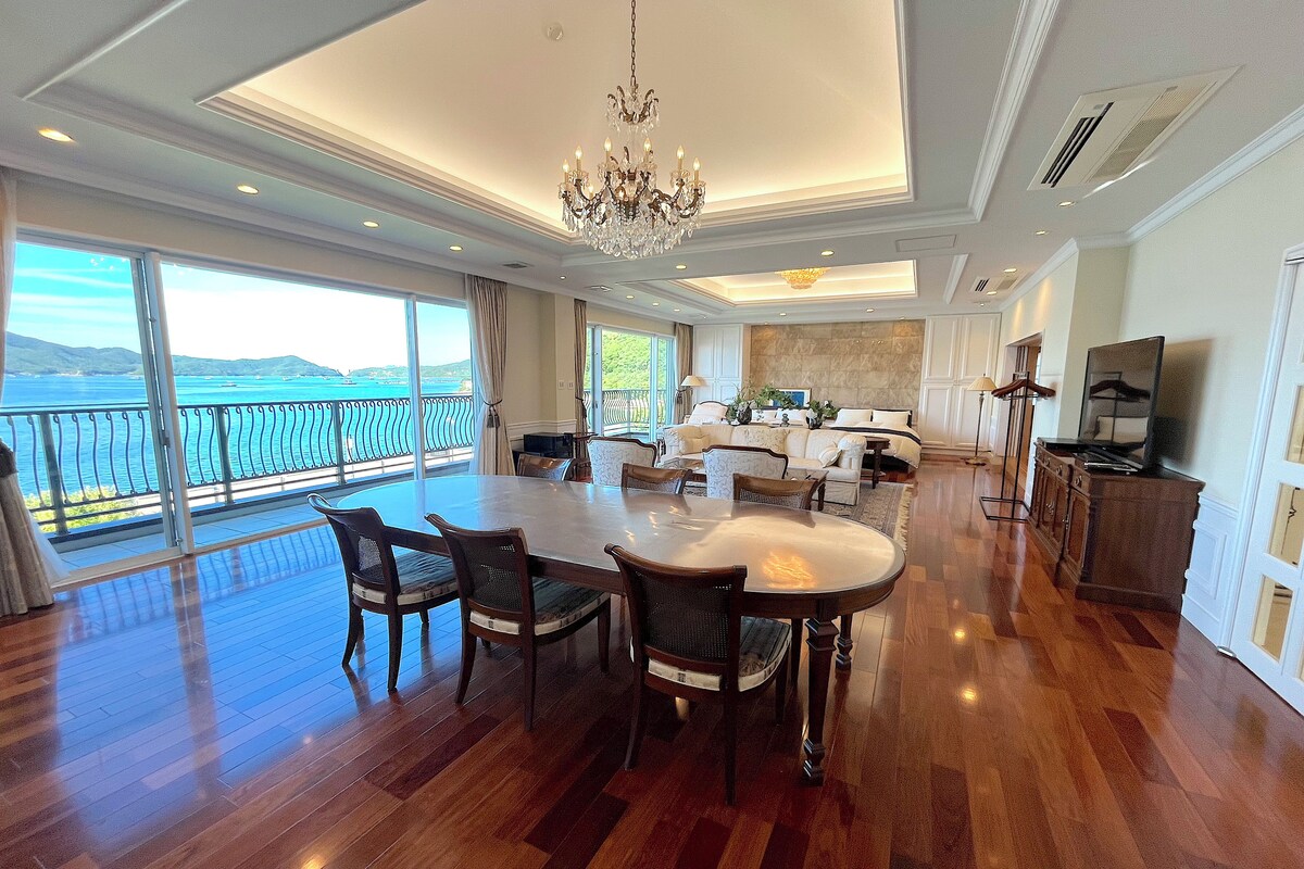A spacious living area with a dining table, seating, and a view of the sea.