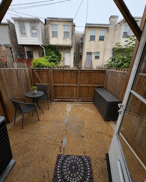 A patio area with a wooden fence, a small table with chairs, and a decorative mat. - A modern artsy 3 bedroom/3.5 bathroom townhome in Baltimore AKA Charm City (Baltimore)