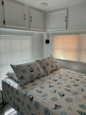 Una camera da letto con un letto, due finestre dotate di persiane e mobili contenitori bianchi sopra il letto.
