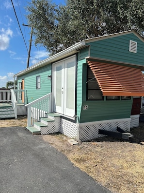 A single-story mobile home with a porch, a door, and a small window. - The Sea Breeze, with Pool Access! (Harlingen)