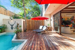 Une terrasse en bois avec une piscine, des chaises longues et un parasol rouge.