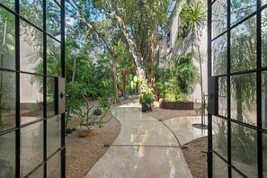 A glass-enclosed garden pathway leading to a wooden structure, surrounded by various plants and trees. - 4BR/4.5 Bath Serviced Villa - Private Pool + Jacuzzi + Staff - BLUE DEER TULUM (Tulum)