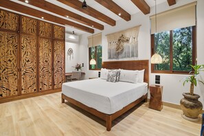 A spacious bedroom with a large bed, wooden ceiling beams, a decorative wall panel, and a view of greenery through the windows. - 4BR/4.5 Bath Serviced Villa - Private Pool + Jacuzzi + Staff - BLUE DEER TULUM (Tulum)