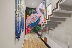 Uma escadaria moderna com guarda-corrimão de vidro, um mural de flamingo na parede e decorações em macramé.