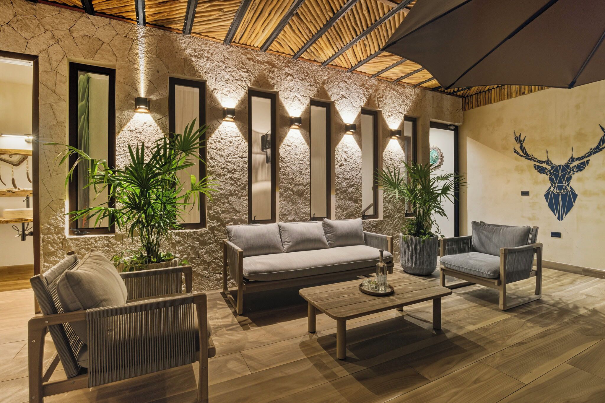 Ein moderner Lounge-Bereich mit einer Steinwand, einer großen Holzbalkendecke und einem aufgehängten Hirsch-Dekor.