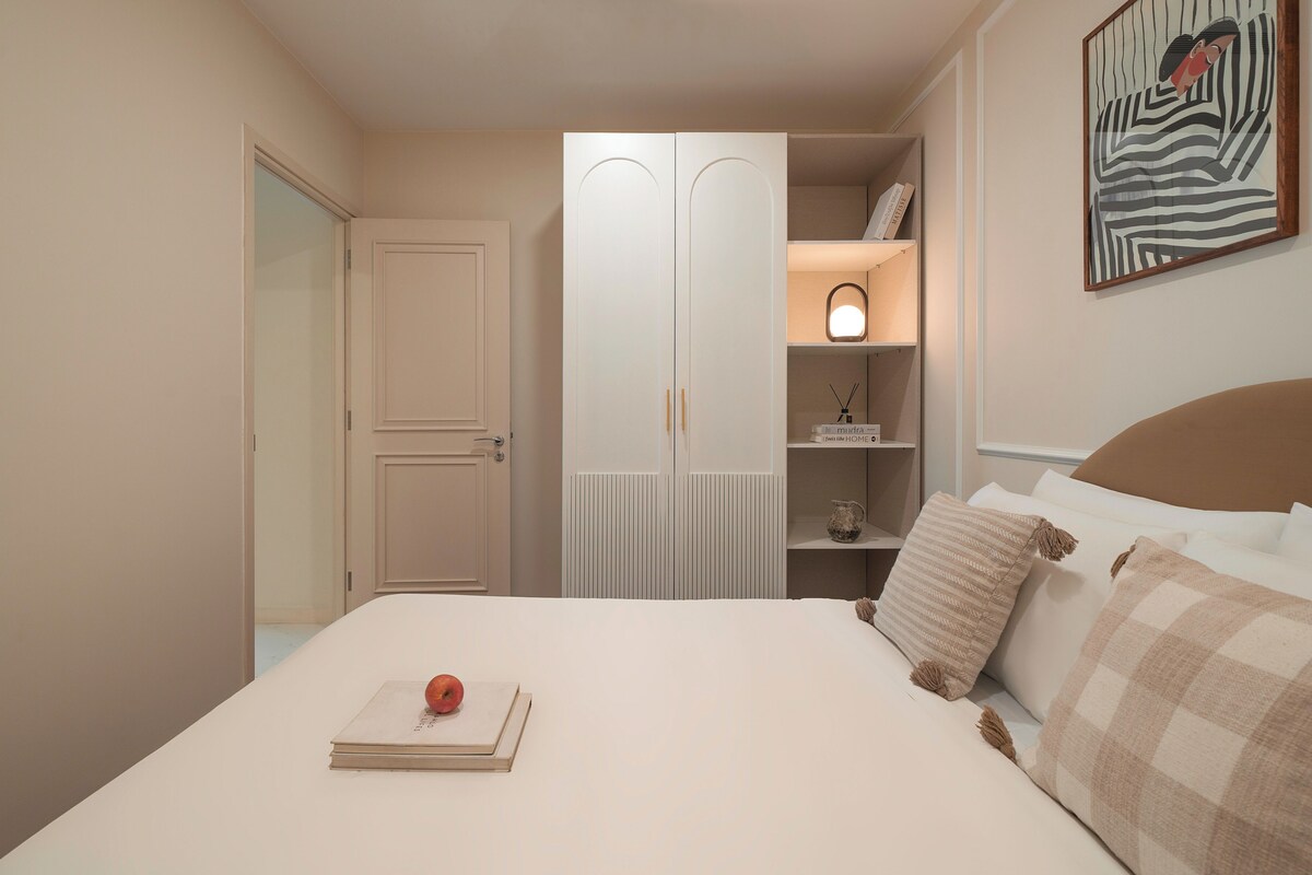A bedroom with a bed, a wardrobe, a bedside table, and a wall-mounted artwork.