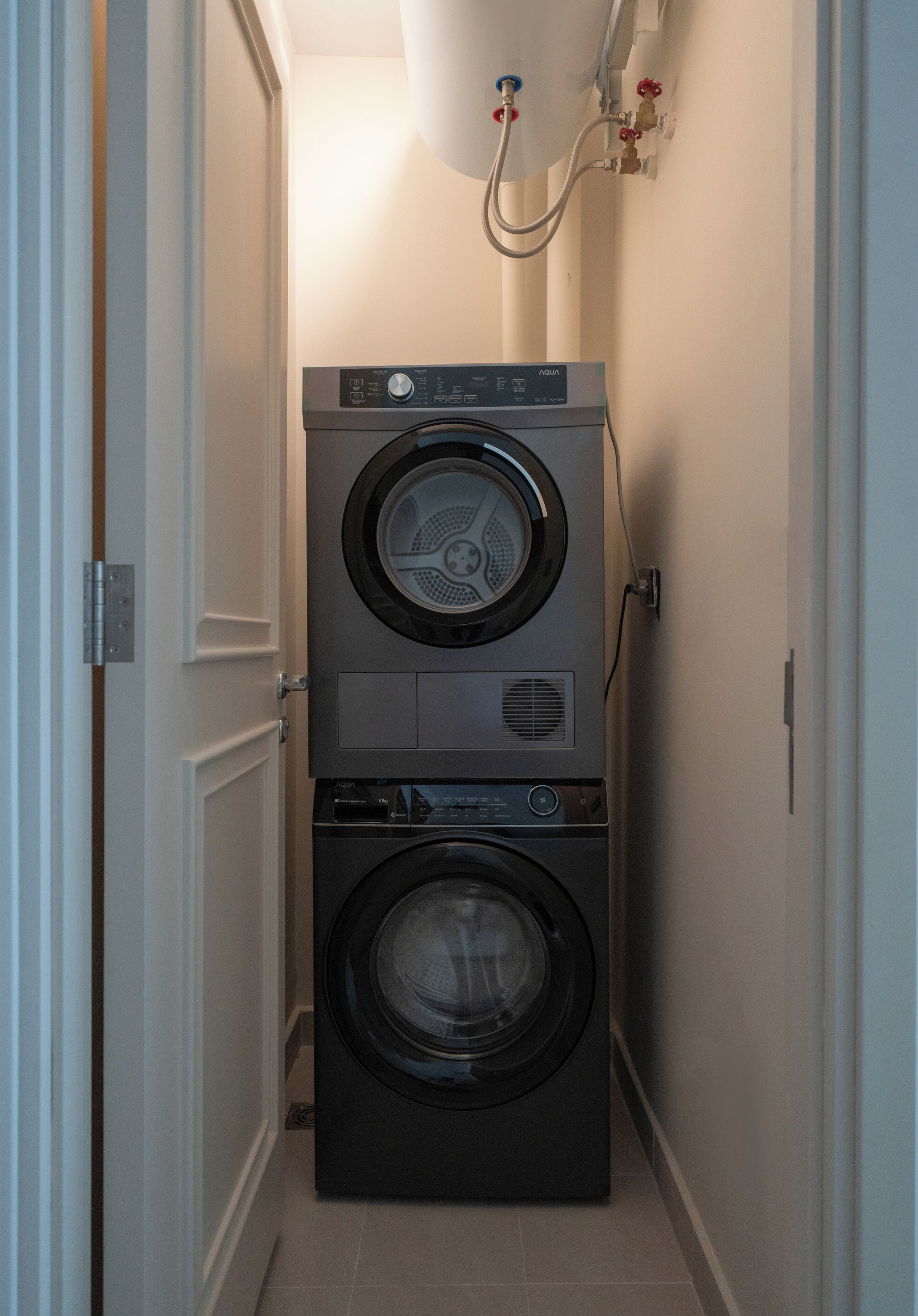 A laundry room with two stacked front-loading washing machines and a water heater above.