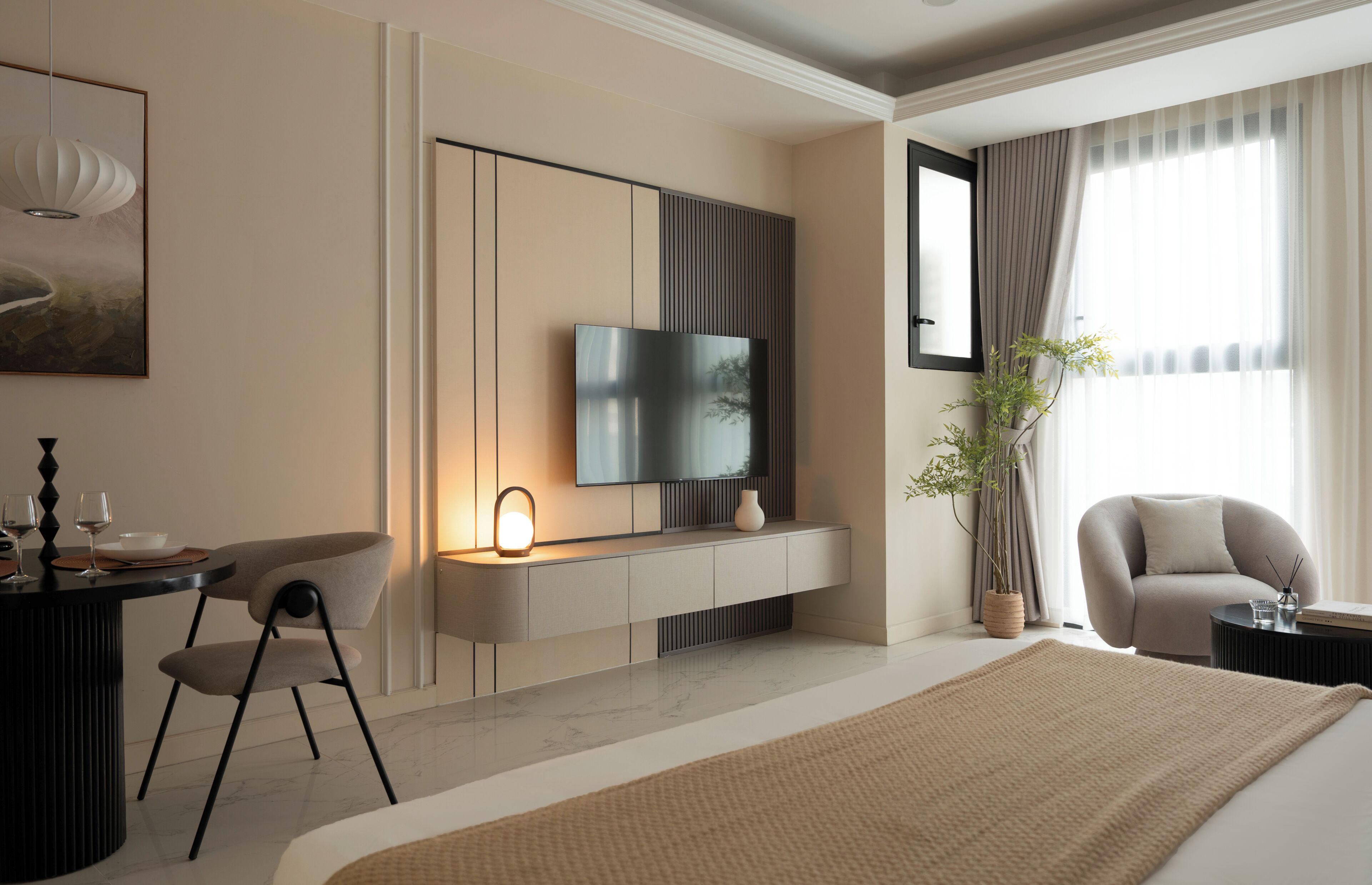 A modern hotel room with a flat-screen TV, a dining area with a table and chairs, a large bed, and a potted plant.