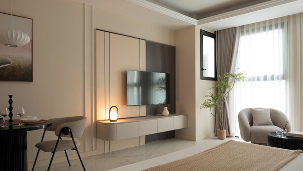 A modern hotel room with a flat-screen TV, a dining area with a table and chairs, a large bed, and a potted plant. - Maison De Gu Thi Sách Apartment (Ben Nghe)