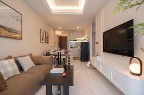 Ein modernes Wohnzimmer mit Sofa, Esstisch, Fernseher und einer Küche im Hintergrund.