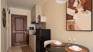 A compact kitchen with a refrigerator, microwave, and a dining area with a table and chairs. - Maison De Gu Thi Sách Apartment (Ben Nghe)