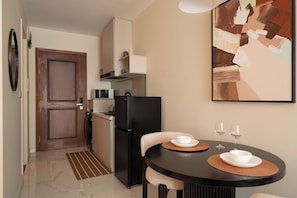 A compact kitchen with a refrigerator, microwave, and a dining area with a table and chairs. - Maison De Gu Thi Sách Apartment (Ben Nghe)