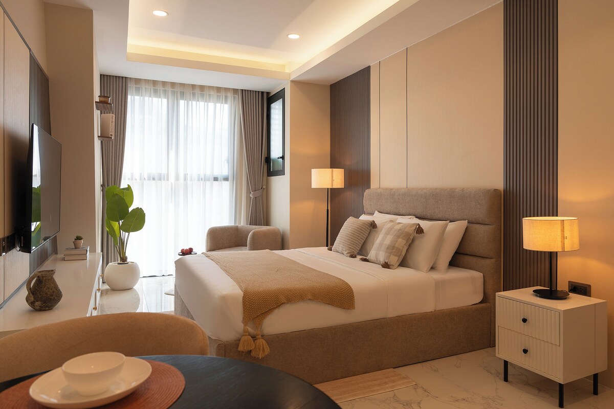 A modern hotel room with a large bed, bedside tables, a TV, and a view of the outdoors.