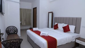 Habitación de hotel con cama, mesita de noche, silla y baño visible al fondo.