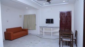 Una habitación con ventilador de techo, televisor montado en la pared, aparador de madera, mesa de comedor con sillas y sofá.