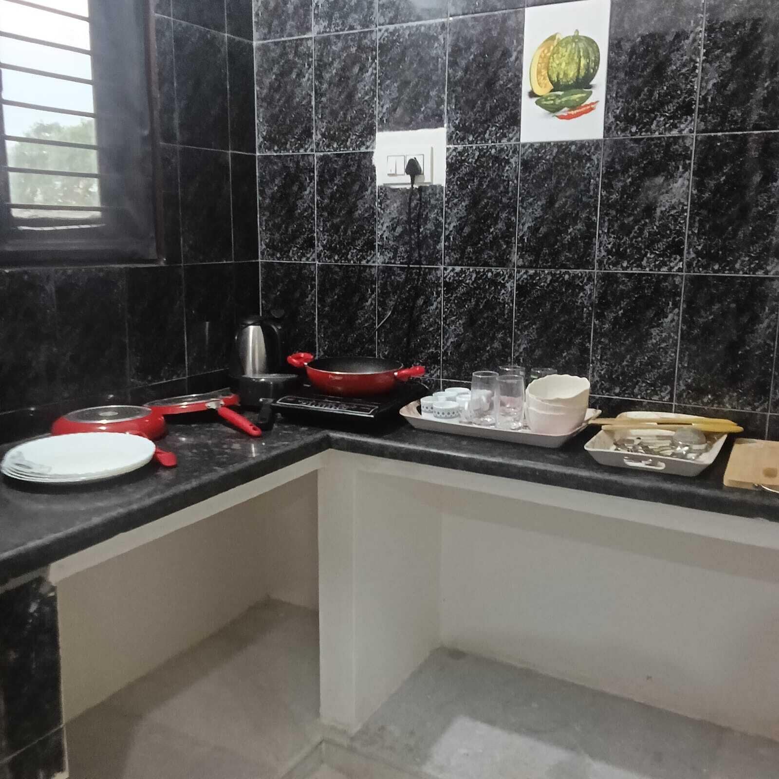 Una cocina con baldosas de mármol negro, una sartén roja, un hervidor y varios utensilios de cocina sobre la encimera.