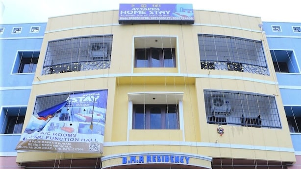 Un edificio de varios pisos con un letrero que anuncia 'B.M.A Residency' y 'Ayyappa Home Stay', ofreciendo habitaciones con aire acondicionado y una sala de funciones con aire acondicionado.