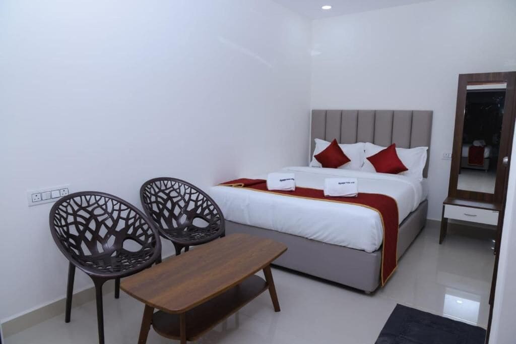 Una habitación de hotel con una cama, dos sillas, una mesita y un espejo.
