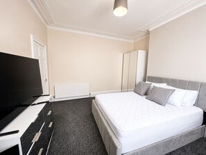 A hotel room with a bed, a television, a radiator, and a wardrobe. - Modern, stylish and comfortable 2-Bed Home, Minutes from Newcastle City Centre (Gateshead)