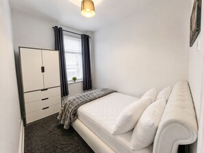 A bedroom with a bed, a wardrobe, a window with curtains, and a small plant on the windowsill. - Modern, stylish and comfortable 2-Bed Home, Minutes from Newcastle City Centre (Gateshead)