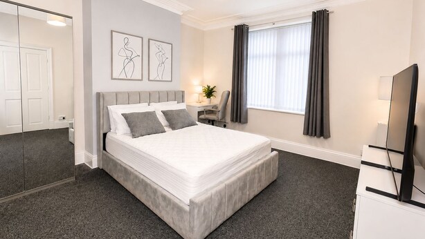 Ein Hotelzimmer mit einem großen Bett, einem Schreibtisch, einem Sessel, einem Fernseher und einem Fenster mit Vorhängen.