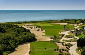 Ein Golfplatz mit mehreren Bahnen, Sandgebieten und Blick auf den Ozean.