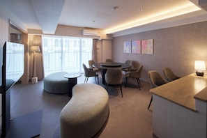 A modern hotel room with a flat-screen TV, a round dining table with chairs, a sofa, and a small kitchenette area. - KOUSA Osaka Namba (Osaka)