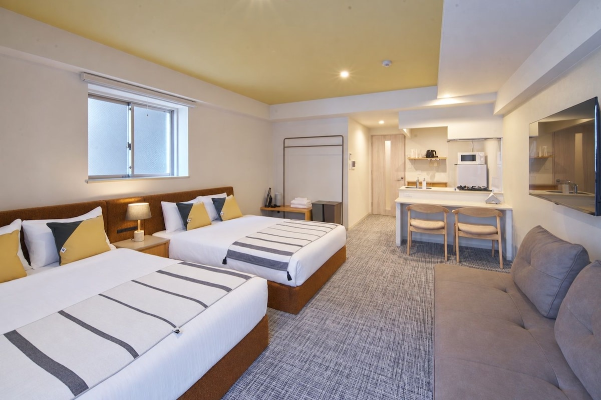 A hotel room with two beds, a desk, a chair, and a sofa.