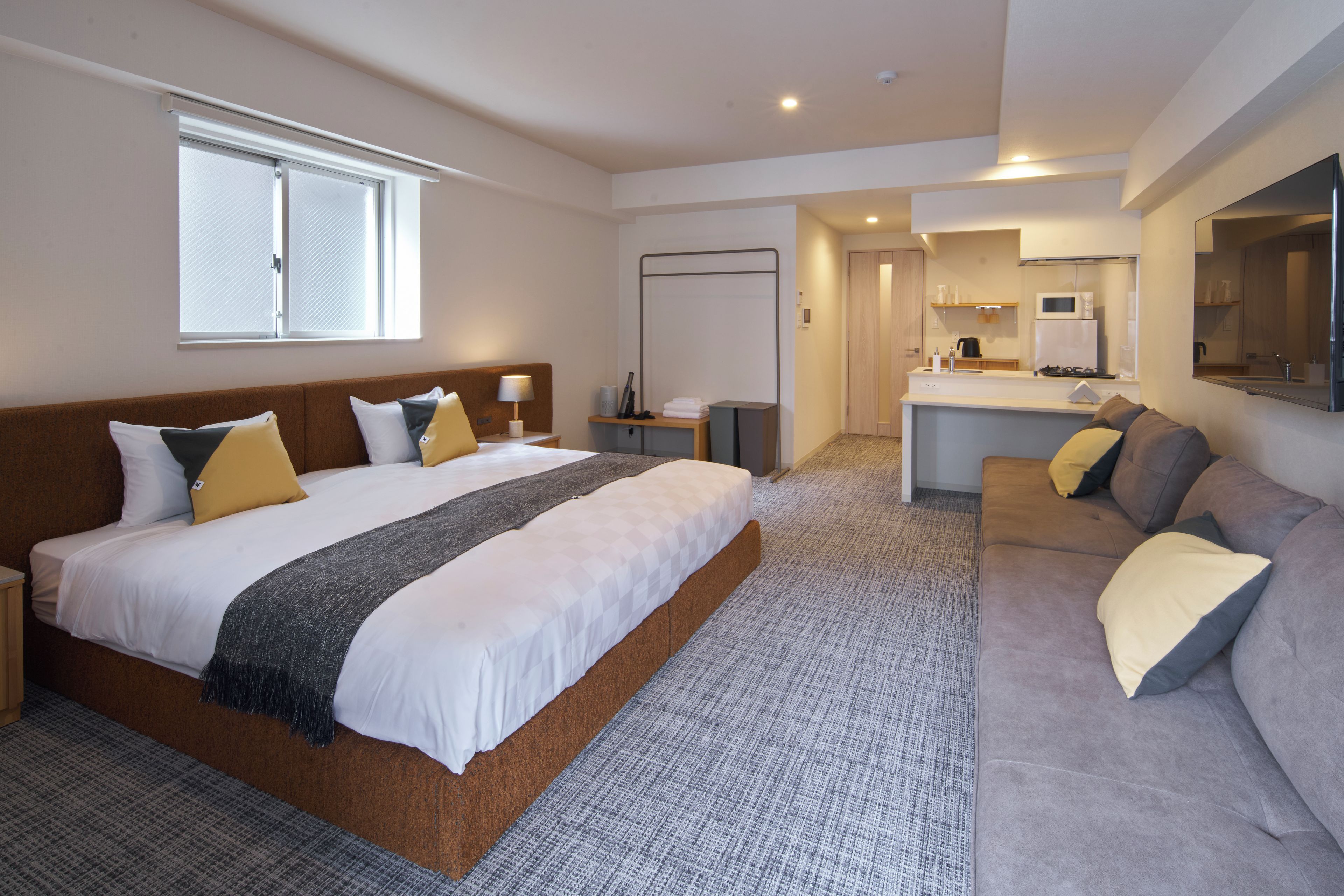 A hotel room with a large bed, a sofa, a kitchenette, and a bathroom.