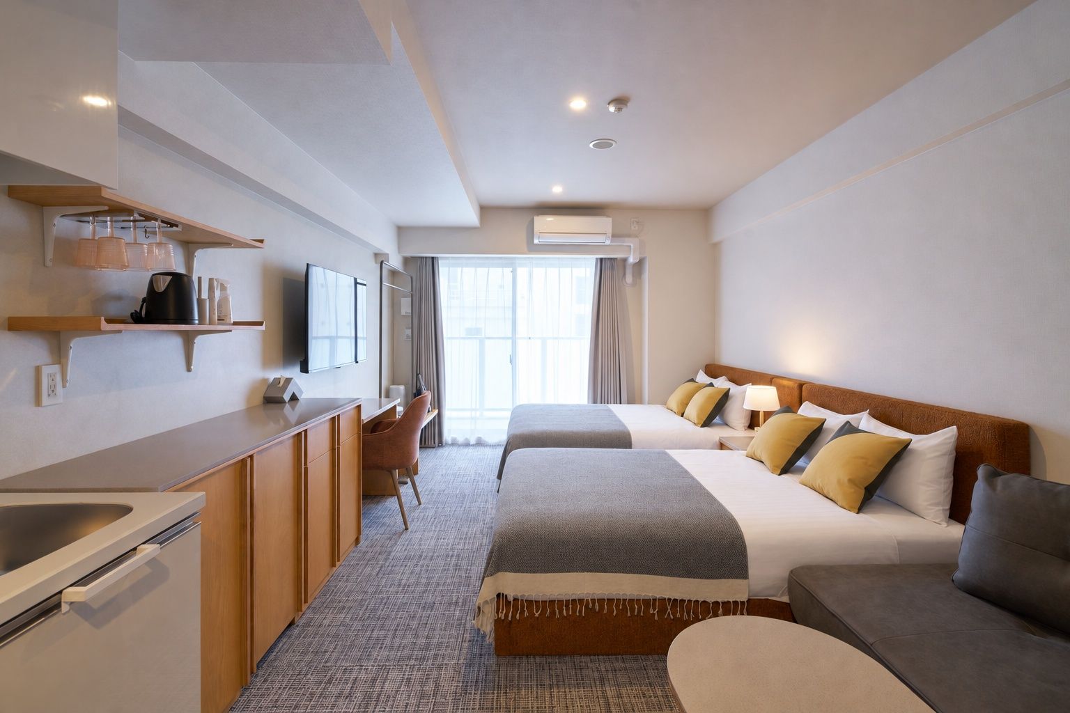 Quarto de hotel com cozinha compacta, cama com muitas almofadas, sofá e televisão.