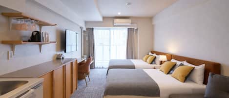 Quarto de hotel com cozinha compacta, cama com muitas almofadas, sofá e televisão.