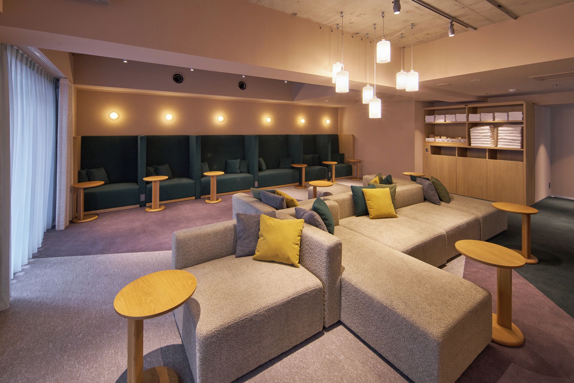 A modern lounge area with sofas and round tables, a wooden cabinet with towels, and pendant lighting.