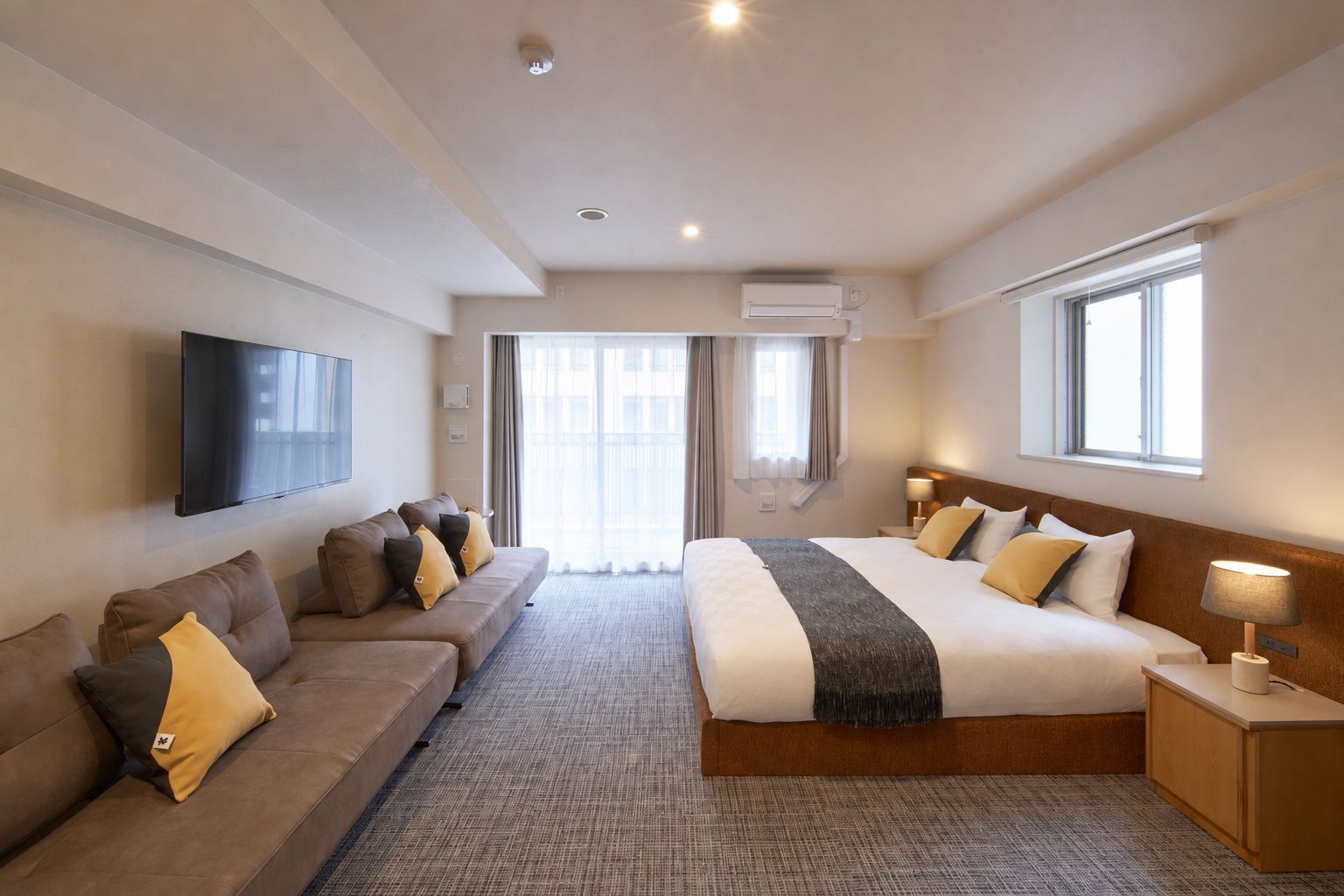 A hotel room with a large bed, a sofa, a TV, and a window.