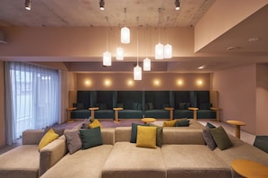 Uma área de estar moderna com sofás e mesas, iluminação pendente e uma grande janela com cortinas.