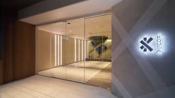 A modern building entrance with a glass door, a wooden wall on one side, and a logo on the wall.