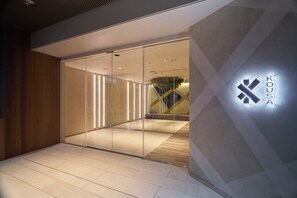 Ingresso di un edificio moderno con porta in vetro, parete in legno su un lato e un logo sul muro.