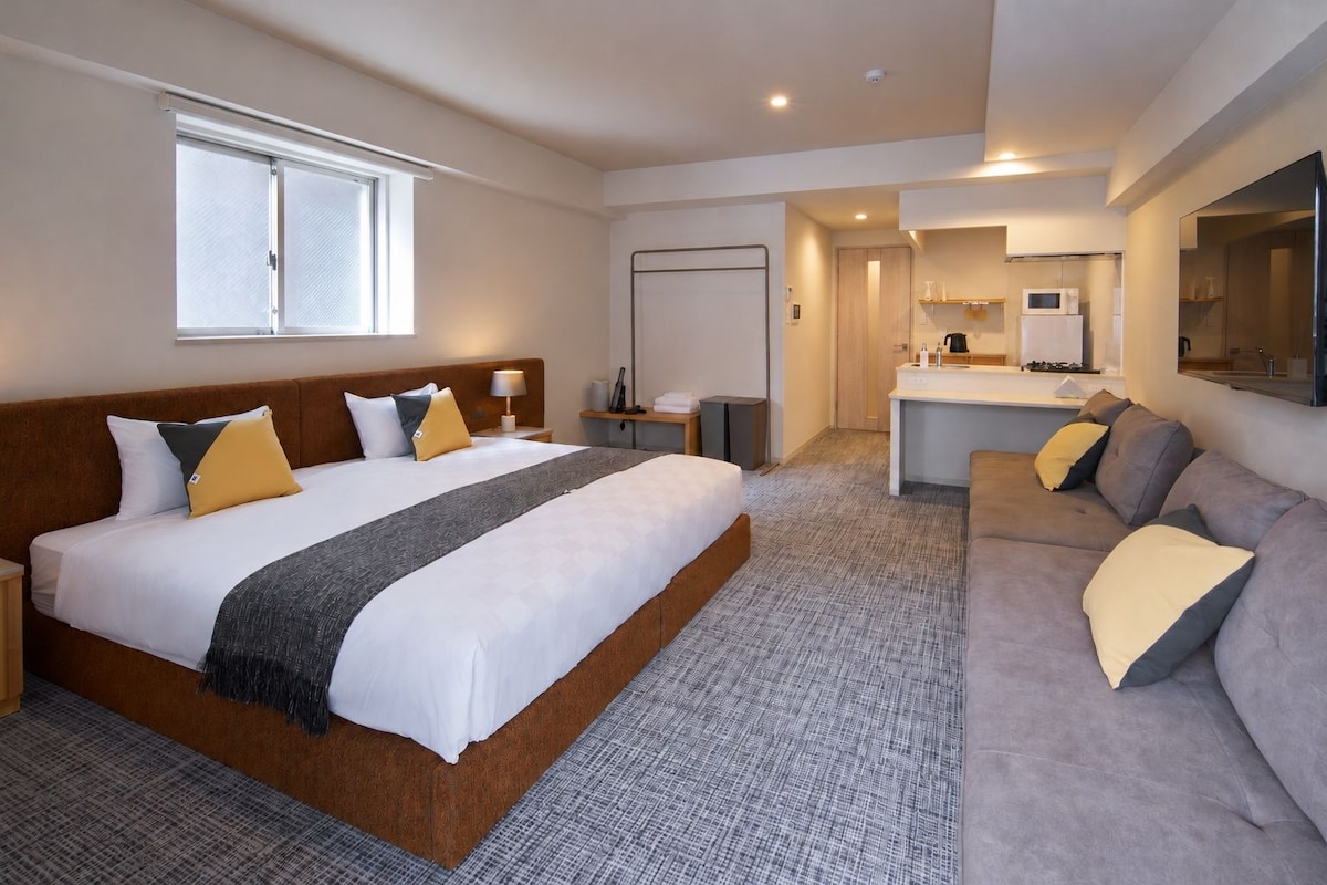 A hotel room with a large bed, a sofa, a desk, and a bathroom.