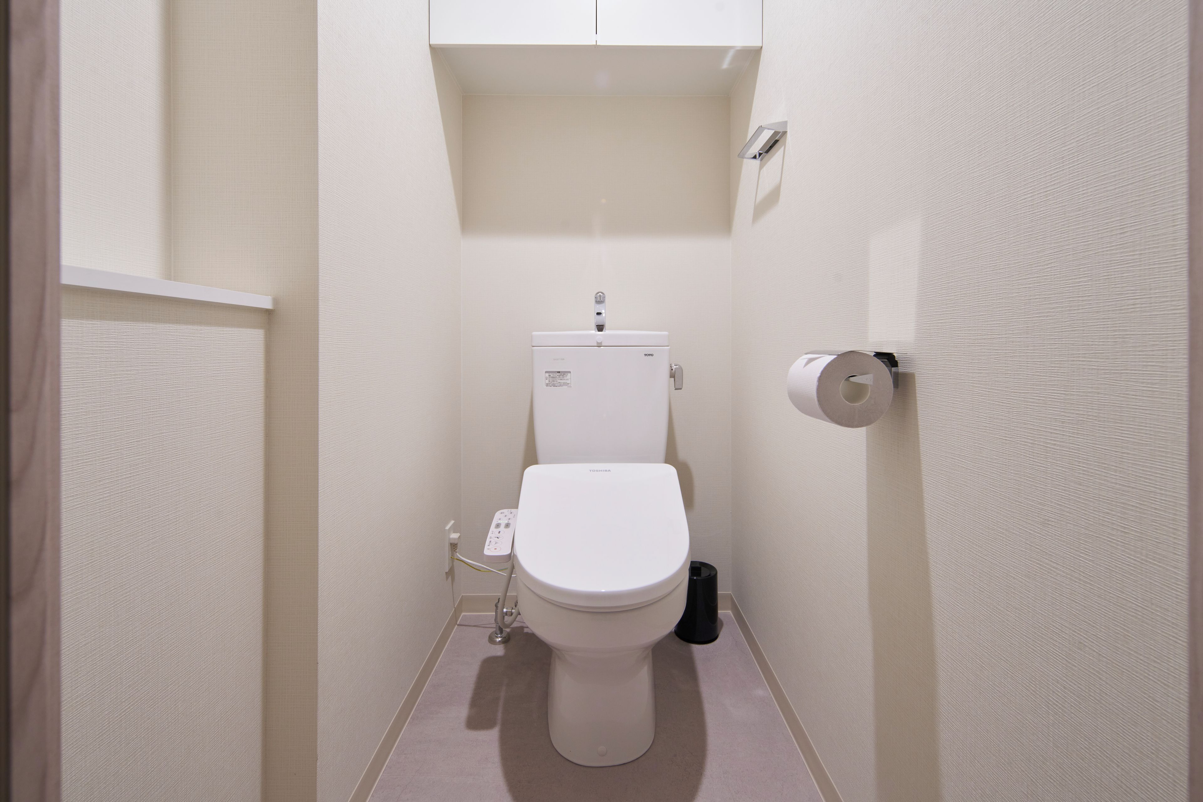 Ein kleines, schmales Badezimmer mit Toilette, Toilettenpapierhalter und sichtbarem Stromanschluss.