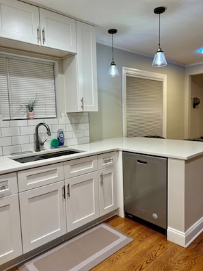 A kitchen with white cabinets, a dishwasher, a sink, and two pendant lights. - Luxury Lincolnwood 3BR 2BA furnished midterm. Utilities and wifi included. (Lincolnwood)