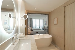 A modern bathroom with a freestanding bathtub, a large mirror, and a vanity with a sink. - Grand Ravindra Hotel & Convention Centre (Sattahip)