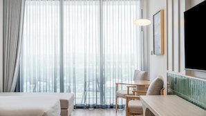 Hotellihuone, jossa on sänky, työpöytä, kaksi tuolia, televisio ja läpikuultavat verhot.