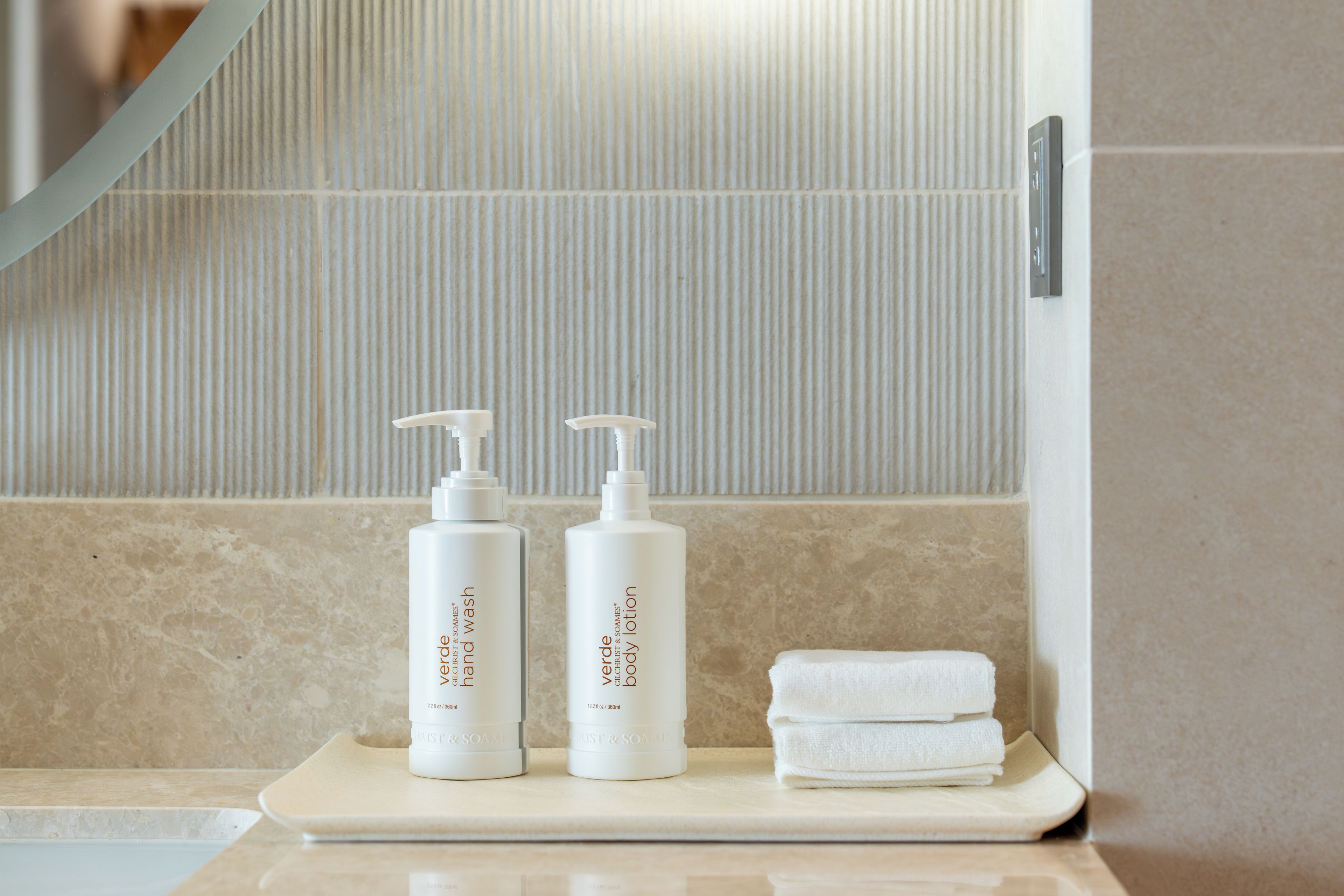 A bathroom counter with two bottles of body lotion and a stack of white towels.