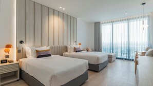 Hotellihuone, jossa on kaksi sänkyä, työpöytä ja suuri ikkuna, jossa on verhot.
