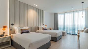 A hotel room with two beds, a desk, and a large window with curtains.