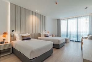 Quarto de hotel com duas camas, uma escrivaninha e uma janela grande com cortinas.