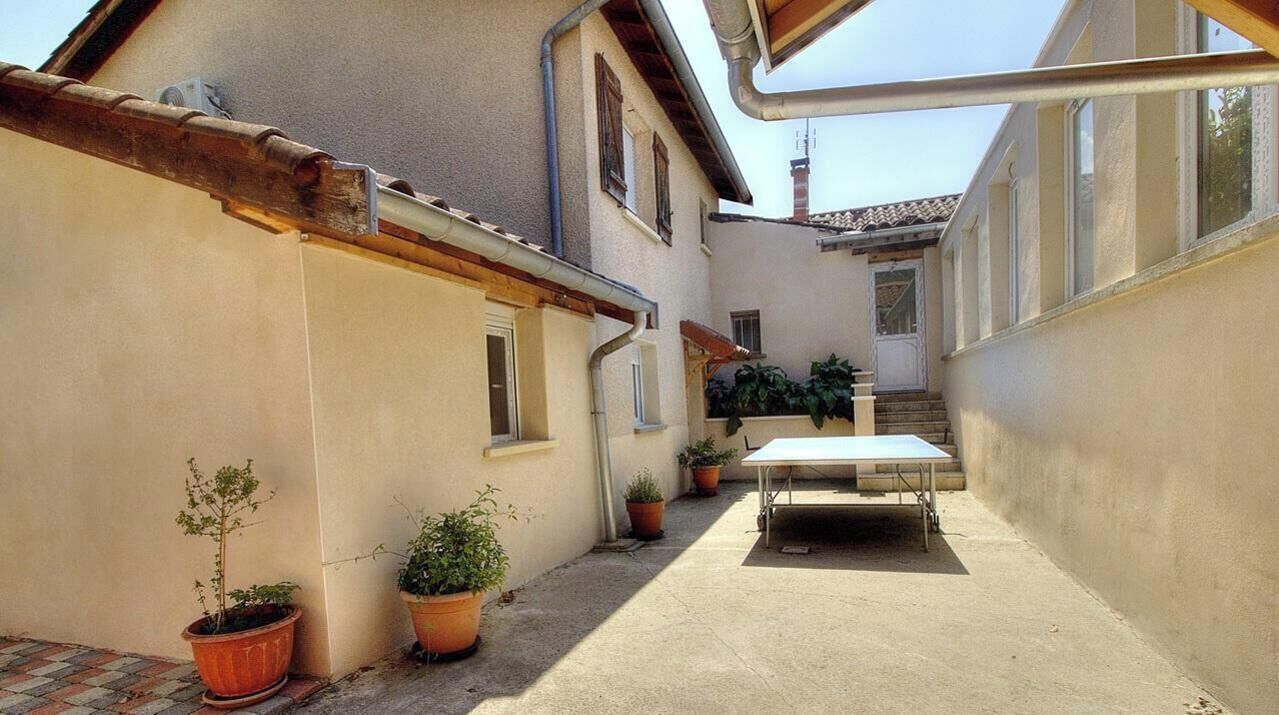 A narrow courtyard with potted plants, a table, and a staircase leading to an upper level.