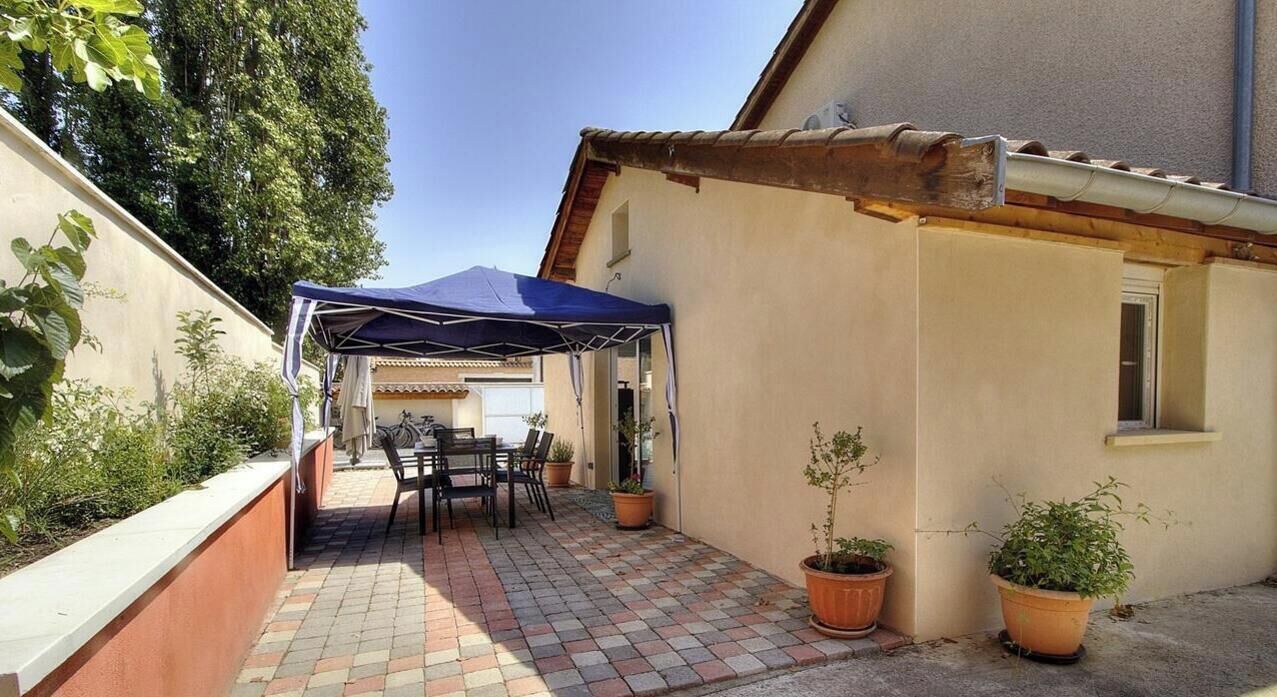 Een terras met een tafel, stoelen, een blauw zonnescherm en potplanten.