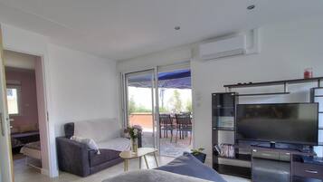 Een moderne woonkamer met een bank, een salontafel, een flatscreen televisie en een schuifpui naar een buitenruimte.