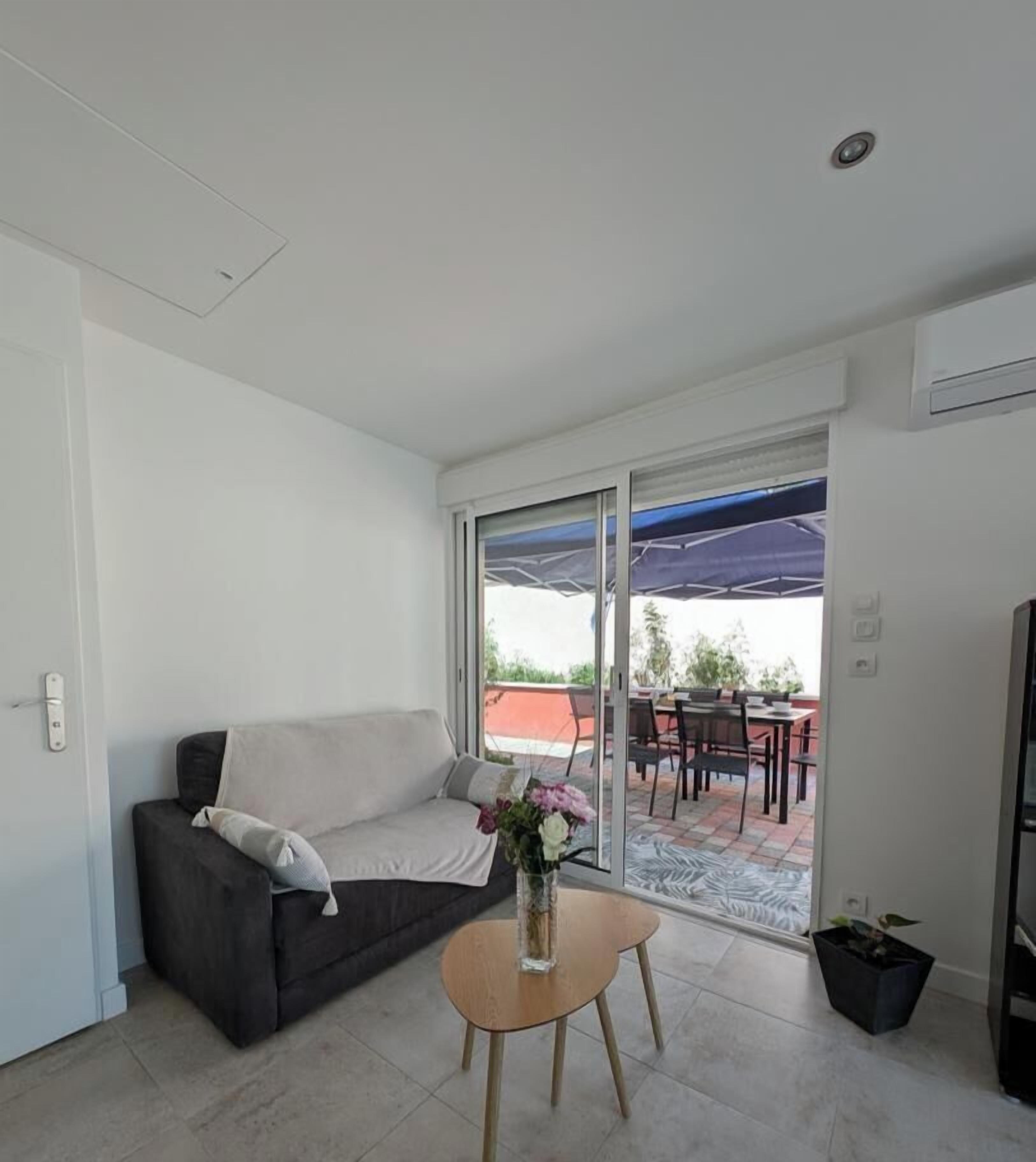 A modern living room with a sofa, a small table, and a view through a glass door to an outdoor patio area.
