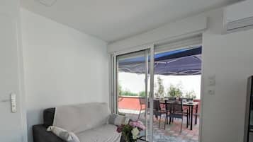 A modern living room with a sofa, a small table, and a view through a glass door to an outdoor patio area.